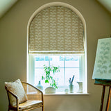 Decorative blind with taupe oakleaf embroidery pattern with a chair and plants.