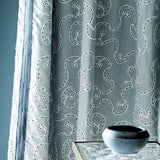 Embroidered blue curtain with a ceramic bowl on a table.