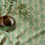 A printed linen fabric sample in green, brown and off white featuring a stylized fern pattern.