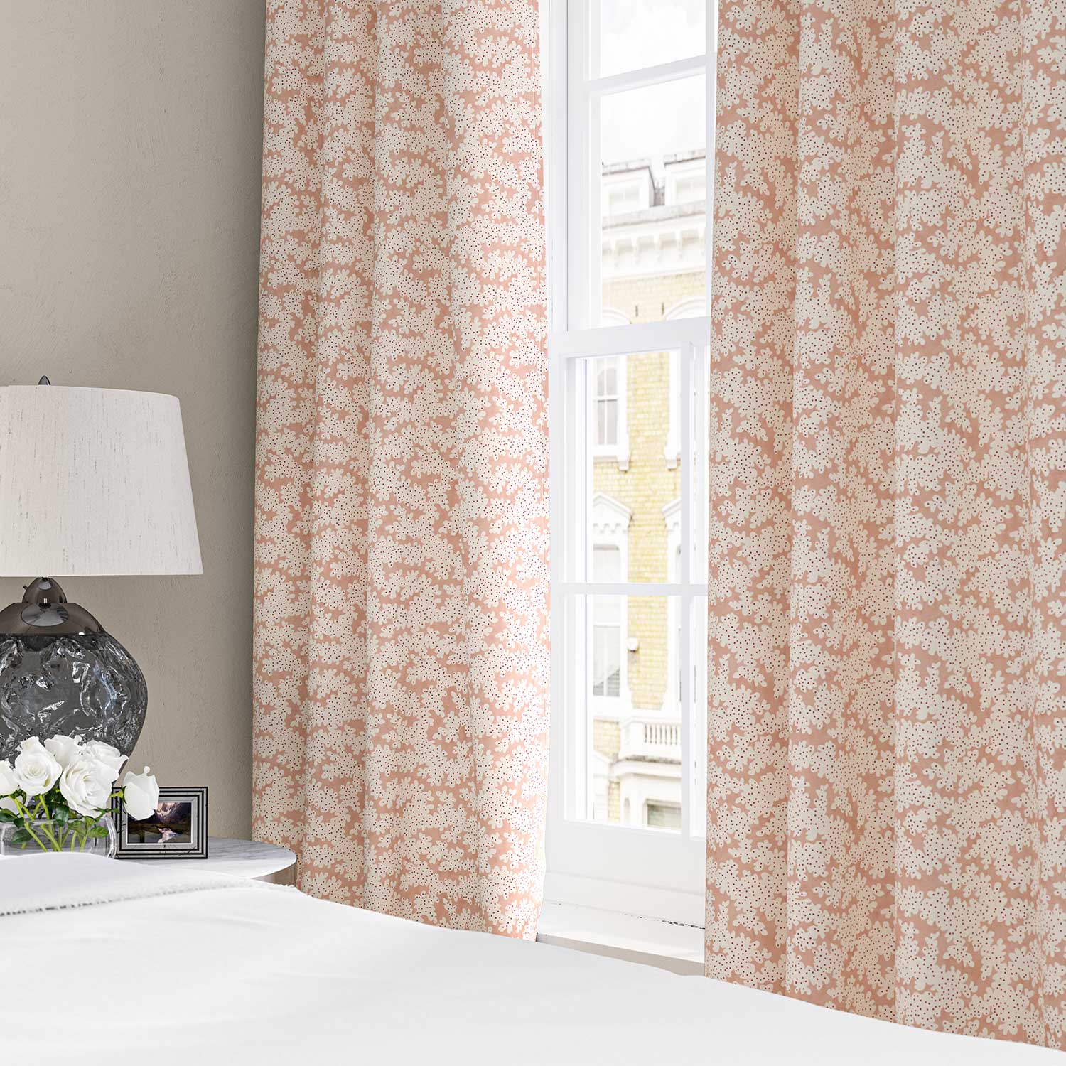 Curtains made from a printed linen fabric sample in pink, red and off white featuring a stylized coral pattern.