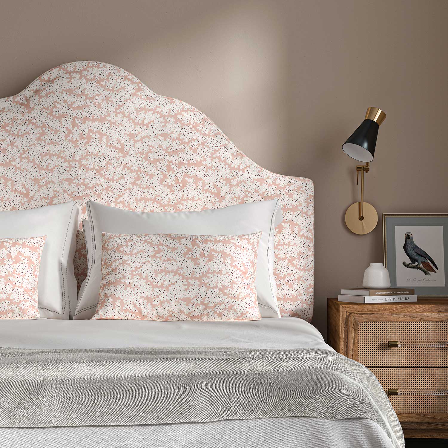 Headboard upholstered in a printed linen fabric sample in pink, red and off white featuring a stylized coral pattern.