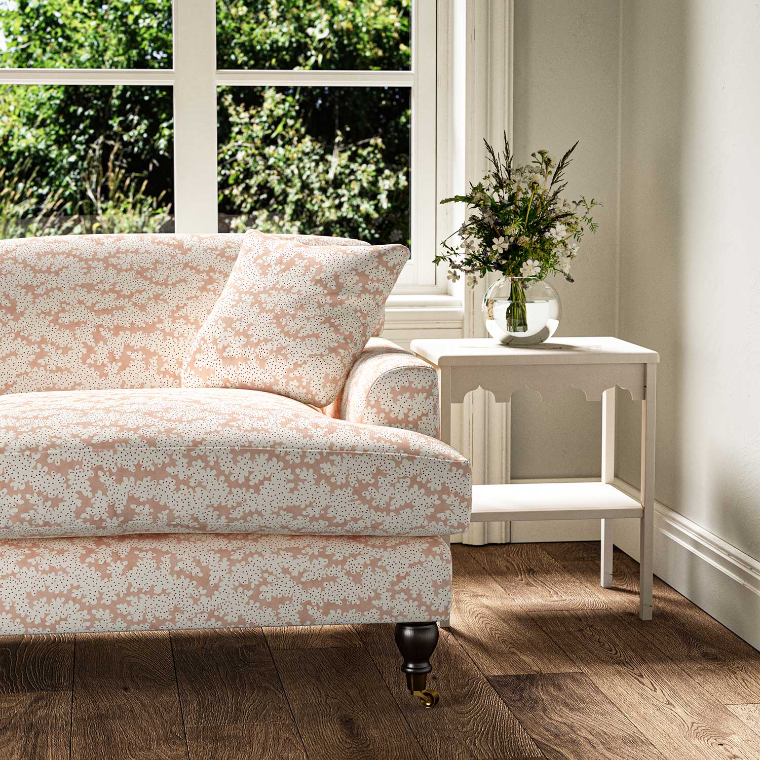 Sofa upholstered in a printed linen fabric sample in pink, red and off white featuring a stylized coral pattern.