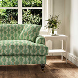 Sofa upholstered in a printed linen fabric sample in green, brown and off white featuring a stylized fern pattern.