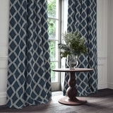 Blue printed velvet curtains with an irregular diamond pattern framing a tall window.