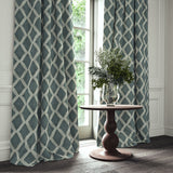Blue printed velvet curtains with an irregular diamond pattern framing a tall window.