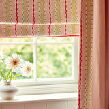 Window with pink embroidered roman blind and curtains, featuring a vase with flowers on a windowsill.
