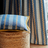 Decorative embroidery pillow with blue and beige pattern on a textured surface with striped curtain in the background.