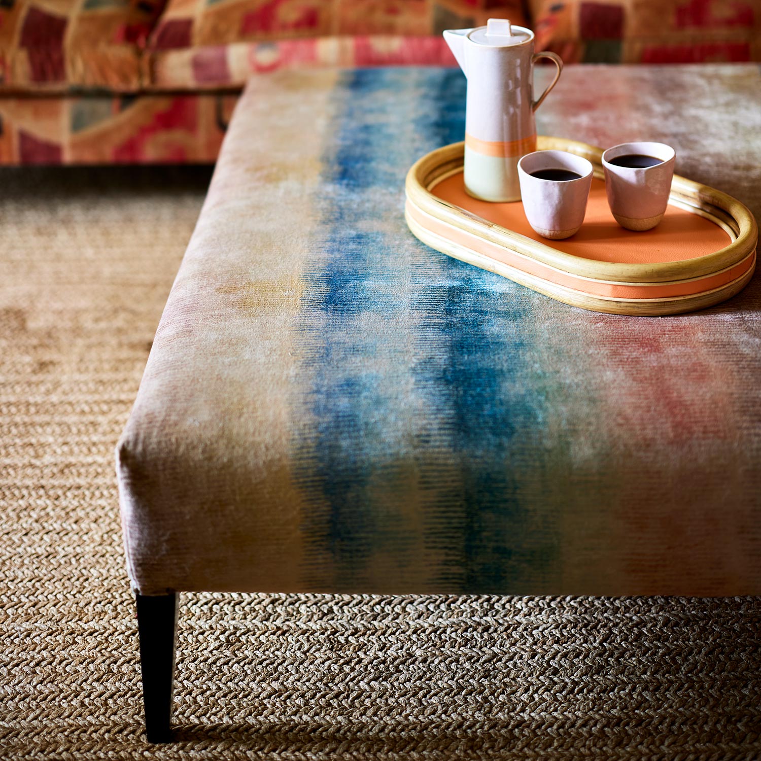 An upholstered footstool in a multicoloured printed velvet with pastel stripes.