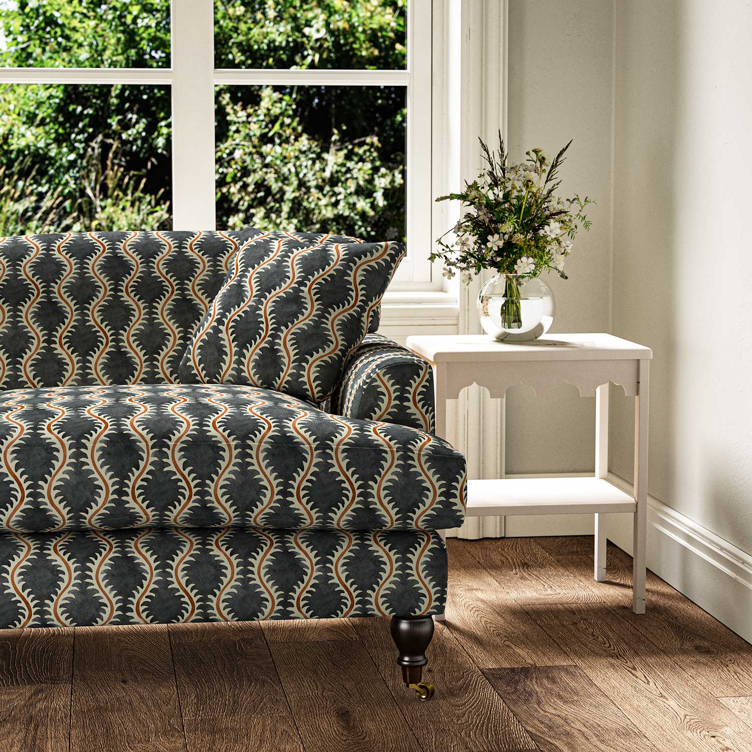 Sofa upholstered in a printed linen fabric sample in blue, orange and off white featuring a stylized fern pattern.