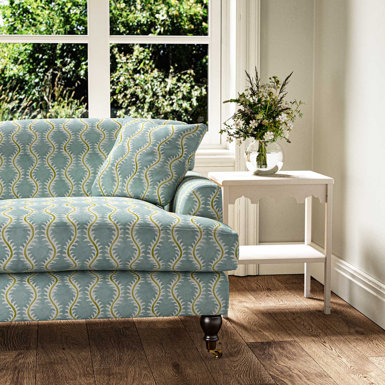 Sofa upholstered in a printed linen fabric sample in blue, green and off white featuring a stylized fern pattern.