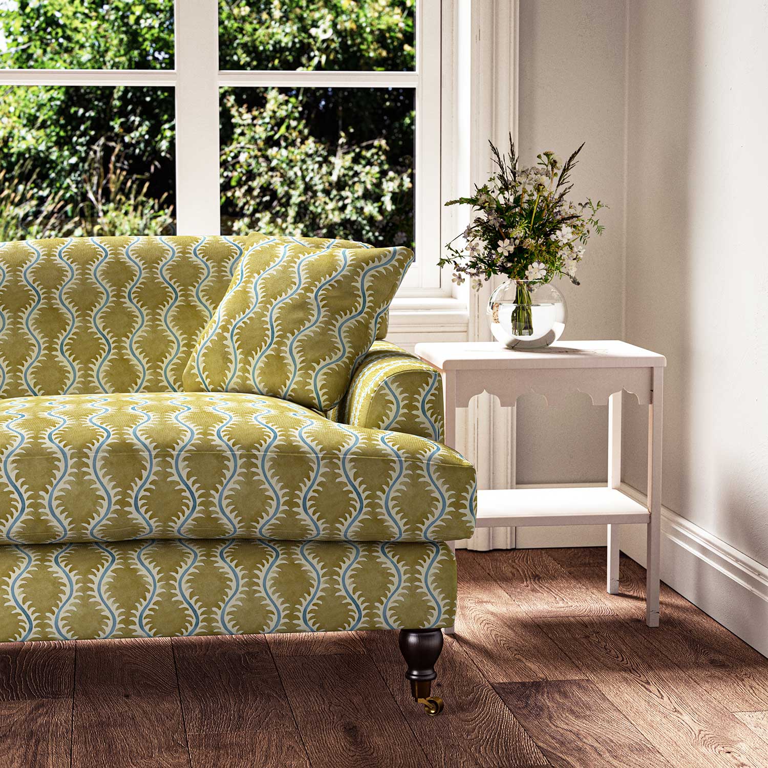 Sofa upholstered in a printed linen fabric sample in yellow, blue and off white featuring a stylized fern pattern.