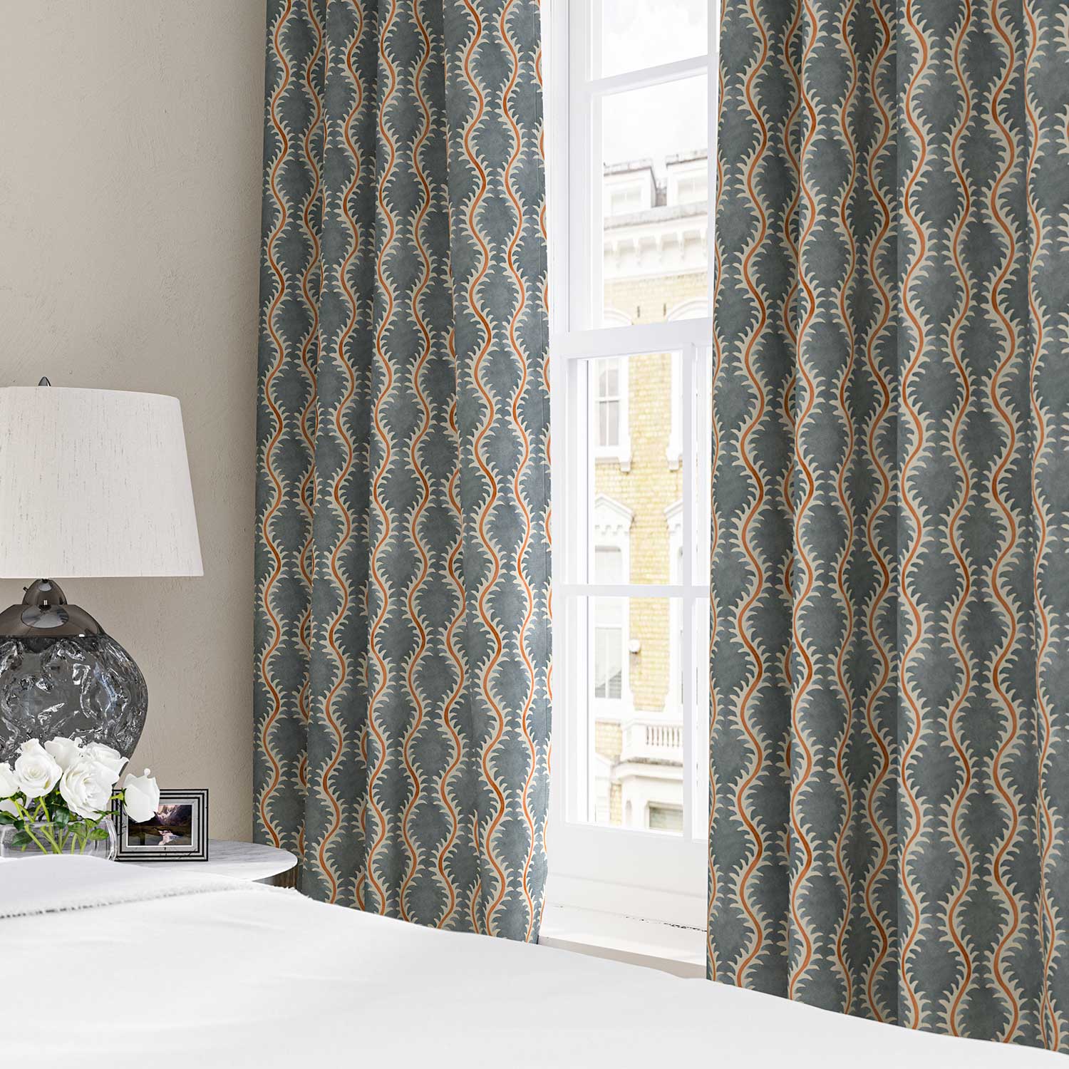 Curtains made from a printed linen fabric sample in blue, orange and off white featuring a stylized fern pattern.
