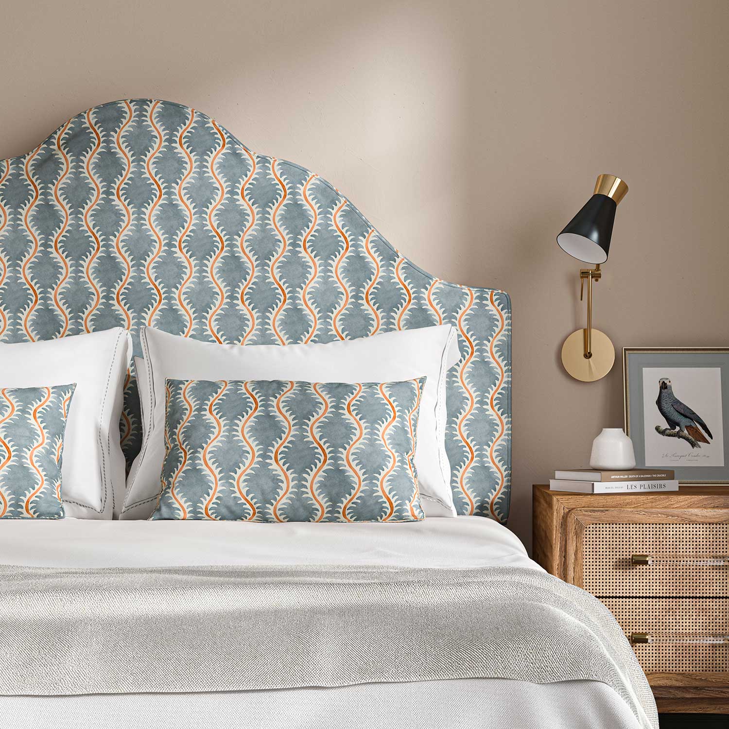 Headboard upholstered in a printed linen fabric sample in blue, orange and off white featuring a stylized fern pattern.