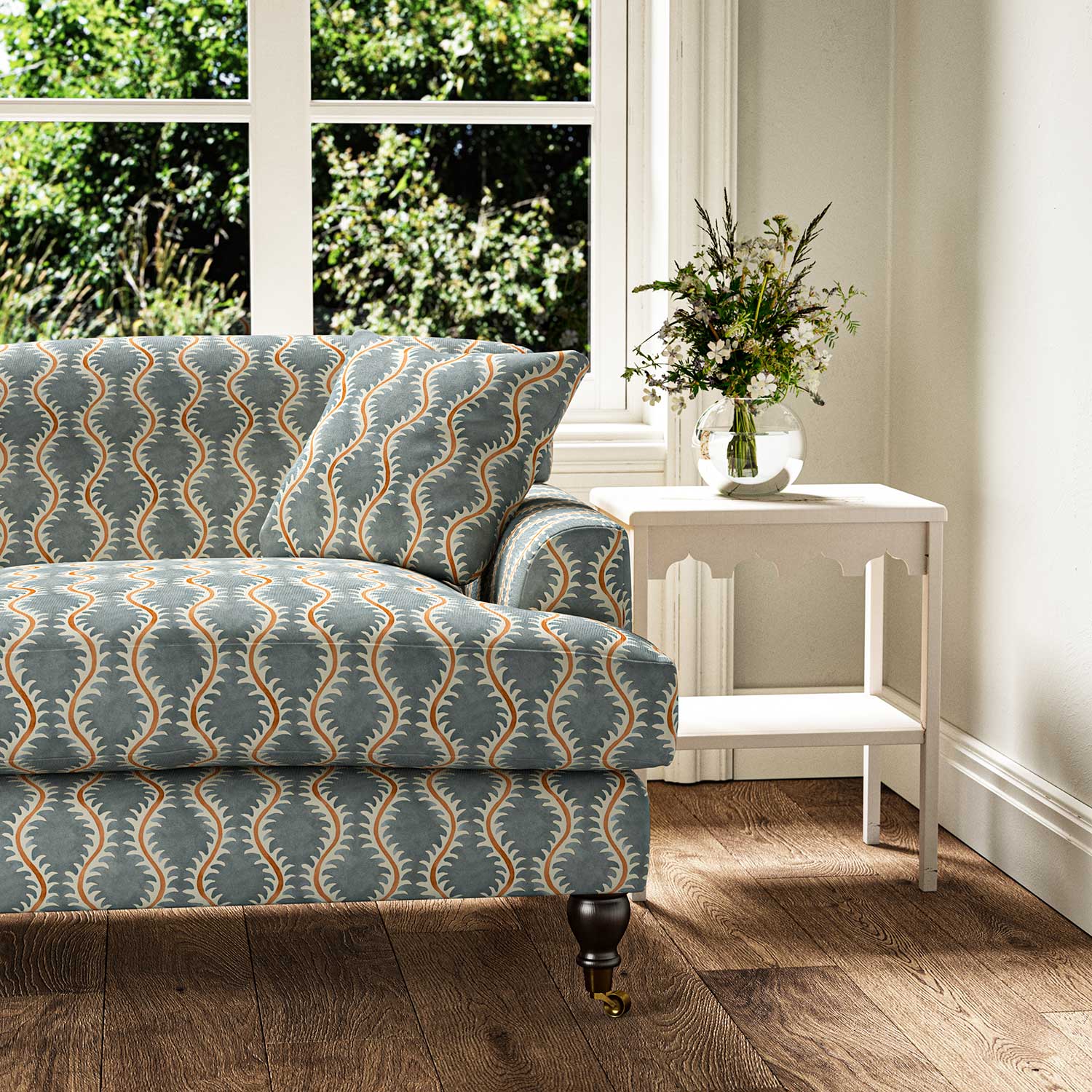 Sofa upholstered in a printed linen fabric sample in blue, orange and off white featuring a stylized fern pattern.