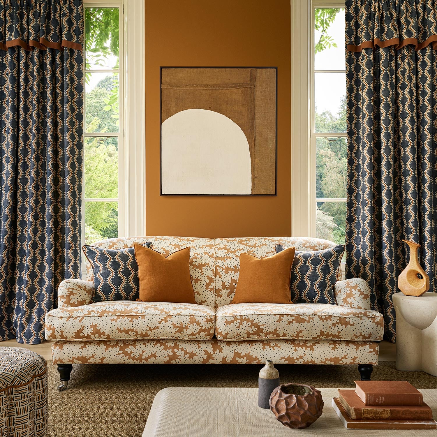 Curtains and cushions made from a printed linen fabric sample in blue, orange and off white featuring a stylized fern pattern.