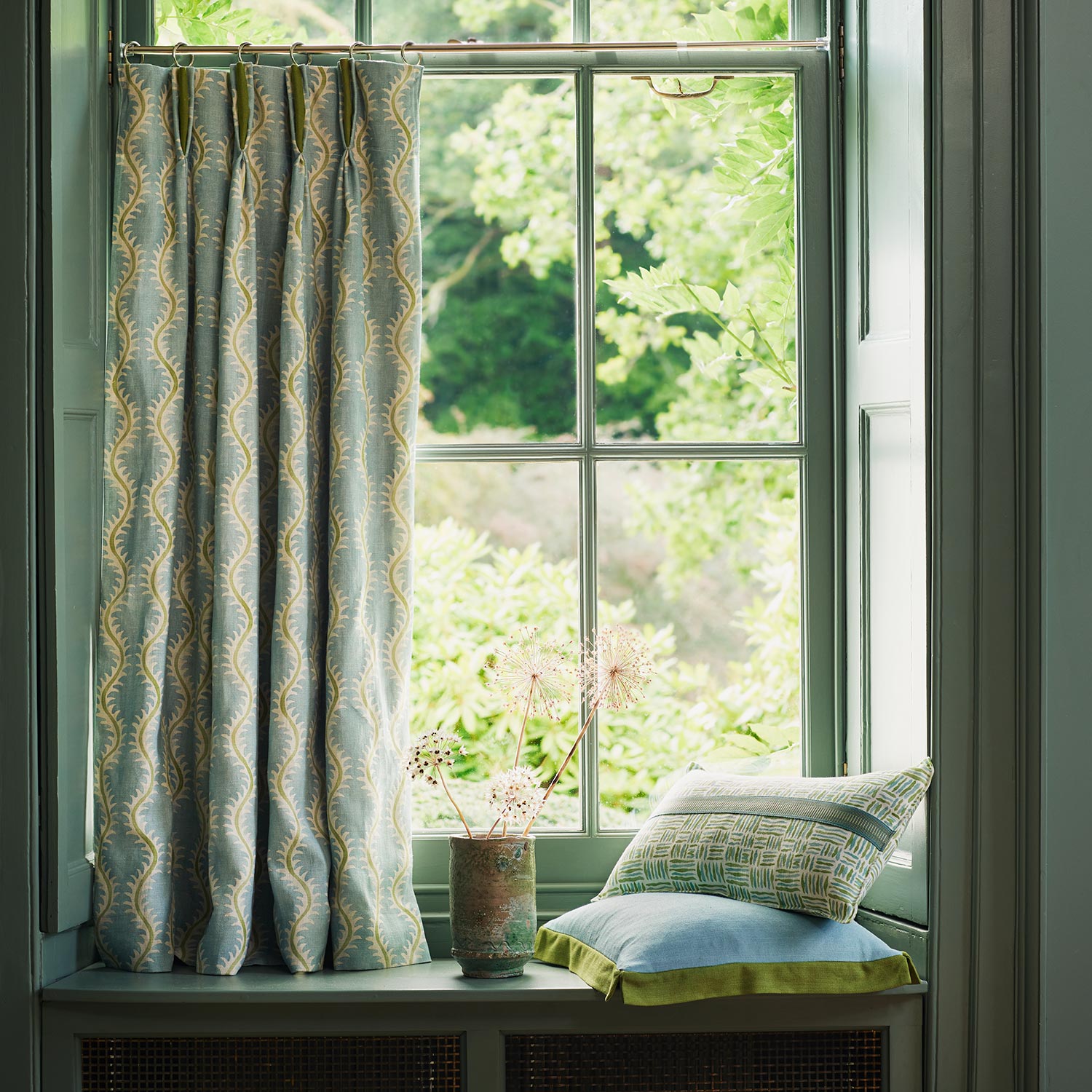 Curtains made from a printed linen fabric sample in blue, green and off white featuring a stylized fern pattern.